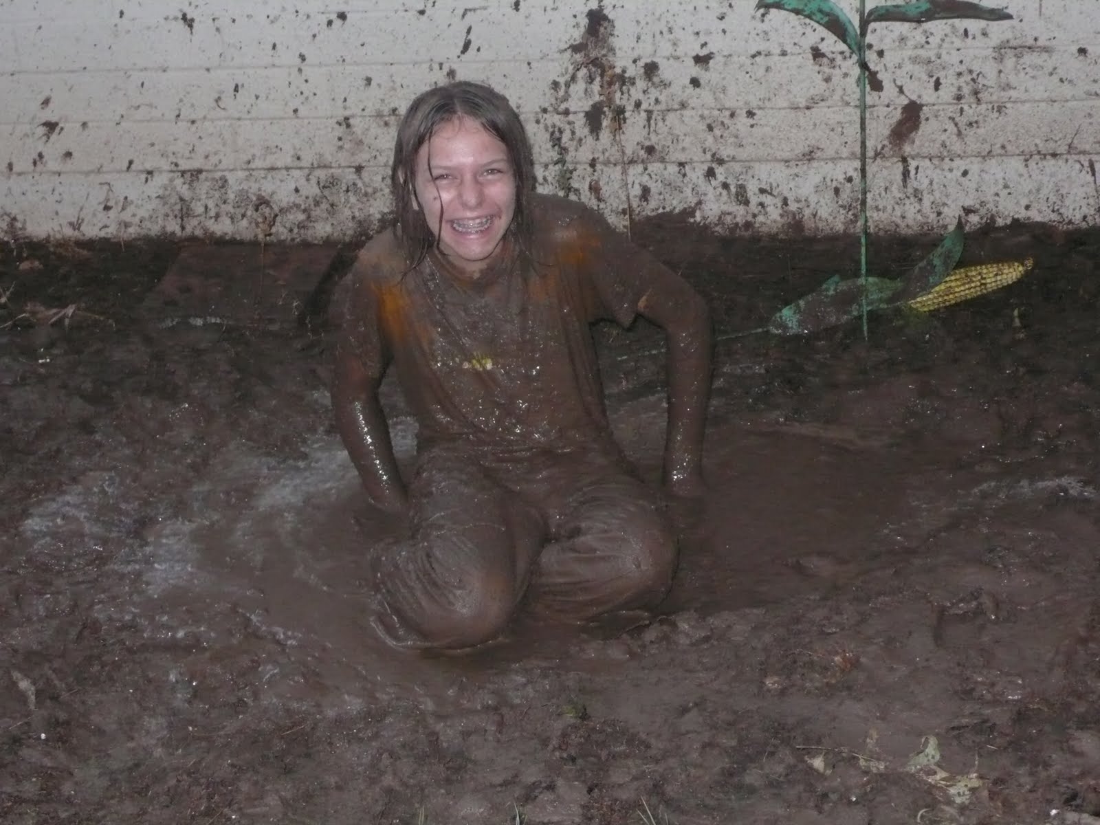 A teenage girl smiles widely because she is caught playing in the mud. She is covered in mud from head to toe.